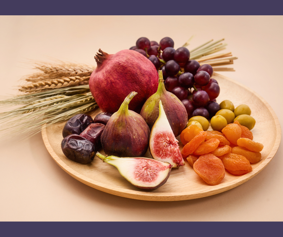 Different fruits, nuts, and seeds, all part of a Tu b'Shvat seder, arranged in a circle on a wooden platter.